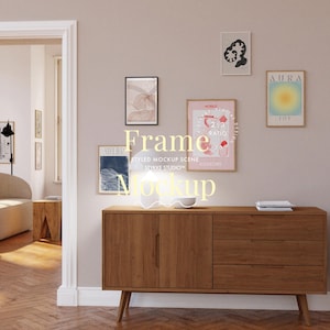 May include: A wooden cabinet with three drawers and two doors. The cabinet is in a living room with a light pink wall and a white lamp on top of the cabinet. There are five framed pictures on the wall above the cabinet. The pictures are of various sizes and colors. The text on the pictures reads "Aura Joy", "Mobile Design Ratio", "Meijer", and "Frame Mockup Scene Stykke Studio".