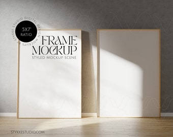 May include: Two empty picture frames with a light wood frame, hanging on a gray wall with a wood floor. The frames are 5x7 inches and the text "FRAME MOCKUP STYLED MOCKUP SCENE" is printed on the left frame.