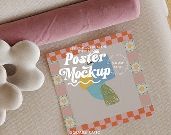 May include: A square poster mockup with a colorful abstract design, featuring the text "Poster Mockup". The poster is surrounded by a pink and orange checkered border. A pink bolster pillow and a white flower-shaped pillow are also in the image.