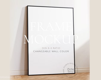 Könnte beinhalten: Ein schwarzer gerahmter Poster-Mockup, der an einer weißen Wand lehnt. Das Poster trägt den Text "FRAME MOCKUP" und "DIN A 4 RATIO CHANGEABLE WALL COLOR". Der Rahmen ist rechteckig und der Hintergrund ist hellbeige.