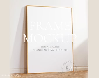 Könnte beinhalten: Ein goldener Rahmen-Mockup mit weißem Hintergrund. Der Rahmen befindet sich an einer weißen Wand und einem Holzboden. Der Text "FRAME MOCKUP" ist in Weiß auf dem Rahmen geschrieben. Der Text "DIN A 4 RATIO" und "CHANGEABLE WALL COLOR" ist in Schwarz unter dem Rahmen geschrieben. Der Text "STYKKE STUDIO DIGITAL DESIGN MOCKUPS" ist in Schwarz auf einem weißen Kreis in der unteren rechten Ecke des Bildes geschrieben.