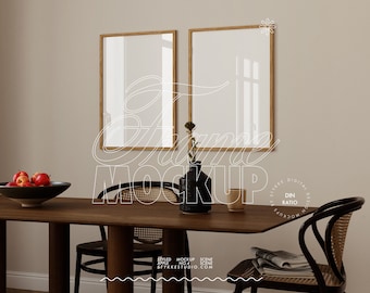 May include: Two wooden framed mirrors hang on a beige wall above a wooden dining table with two chairs. A vase with a green plant sits on the table with a cup and a bowl of red apples.