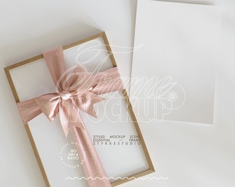 May include: A wooden frame with a pink ribbon tied in a bow. The frame is on a white surface. The text "STYLED MOCKUP SCENE ESSENTIAL FRAME STYKKESTUDIO" is printed on the frame.