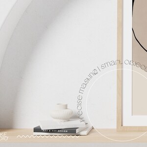 May include: A white ceramic vase with a ribbed texture sits on a stack of books with the text "ANA & VIV DESIGN" on the top book. The books are on a light wood shelf in front of a white wall with an archway. A framed abstract art print with a beige background and black lines hangs on the wall.