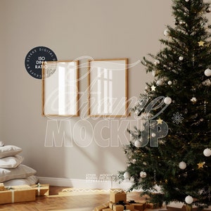 Può includere: Due cornici per foto in legno con passepartout bianchi appese a una parete beige. In primo piano un albero di Natale decorato con palline bianche e luci. L'albero è accanto a una pila di regali avvolti.
