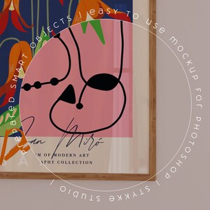 Puede incluir: Un cuadro enmarcado con un dise&ntilde;o abstracto colorido de Joan Mir&oacute;. La obra de arte incluye un fondo rosa con formas y l&iacute;neas negras, y elementos florales naranjas y verdes. El marco es de madera.