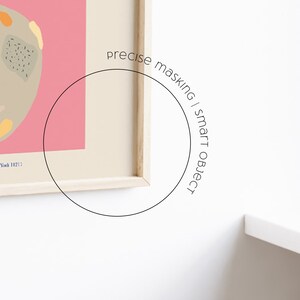 May include: A framed abstract art print with a pink background and a beige shape with colorful accents. The print is in a wooden frame and is hanging on a white wall. The text "precise masking | smart object" is written in a circle around the frame.