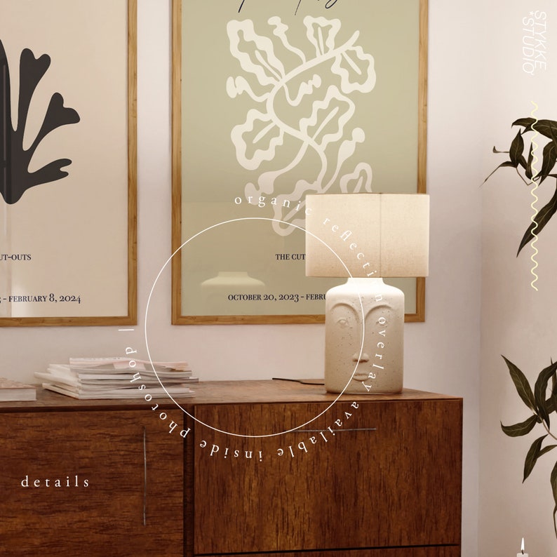 May include: A white ceramic table lamp with a face design and a white fabric shade. The lamp is on a wooden table with a stack of magazines and two framed prints with black and white illustrations. The text on the prints reads "The Cut" and "JT-OUTS".