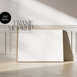 May include: A gold frame mockup scene with a white background and wood floor. The frame is 7x5 inches and is leaning against a white wall with decorative molding. The frame is empty and ready for your design.