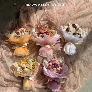 Peut inclure: Cinq petits bouquets de fleurs séchées enveloppés dans du papier de soie de différentes couleurs. Les bouquets sont disposés sur un fond de tissu brun clair. Le texte "ROSYVALLEY DESIGN" est visible en haut de l'image.