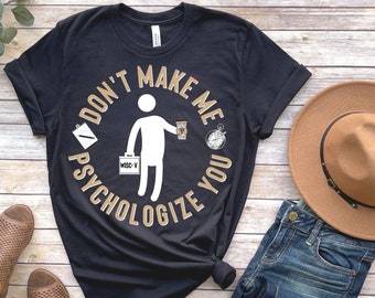May include: Black t-shirt with a gold circle graphic that says "Don't Make Me Psychologize You". The graphic includes a stick figure holding a cup of coffee, a clipboard, a stopwatch, and a briefcase that says "WISC-V".