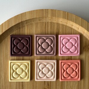 May include: Six ceramic tiles with a raised flower design in different colors. The tiles are brown, pink, light pink, yellow, peach, and orange.
