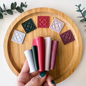 May include: Five silicone teethers in different colors, including red, green, pink, and purple. The teethers are shaped like a flower and are arranged on a wooden tray.