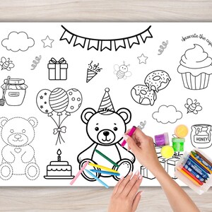 Op de afbeelding: Een witte kleurplaat met illustraties met een verjaardagsthema, waaronder een teddybeer, taart, ballonnen en cupcakes. De tekst "decorate the cupcake" is zichtbaar. Een hand houdt een roze kleurpotlood vast, klaar om te kleuren.