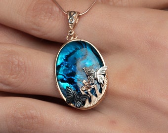 May include: A gold chain necklace with a blue oval pendant featuring a delicate butterfly design. The pendant is made of abalone shell and has a shimmering iridescent finish.