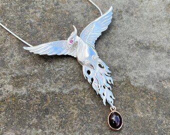 May include: A silver phoenix necklace with a red gemstone eye and a black gemstone pendant.