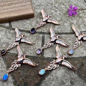 May include: Six silver and rose gold phoenix pendants with different coloured gemstones. The gemstones are amethyst, opal, moonstone, garnet, and two opals.