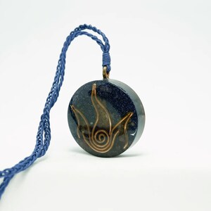 May include: A blue and gold necklace with a round pendant featuring a stylised flame design. The pendant is made of resin and has a glittery finish.
