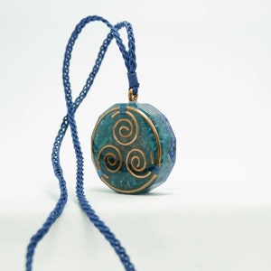 May include: A blue and green stone pendant with a copper wire design in the shape of a triple spiral. The pendant is hanging from a blue cord.