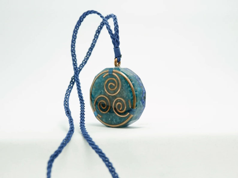 May include: A blue and green stone pendant with a copper wire design in the shape of a triple spiral. The pendant is hanging from a blue cord.