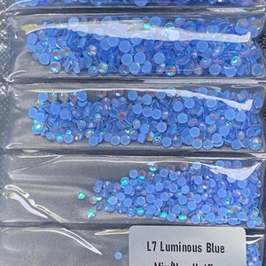 May include: Four rows of light blue iridescent rhinestones in clear plastic packaging. The label reads "L7 Luminous Blue Mix/Non Hotfix 1440pcs".