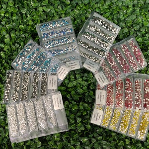 May include: Assortment of clear plastic containers filled with various colours of small round rhinestones. The containers are labelled with the size and quantity of rhinestones.