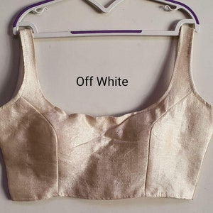 Peut inclure: Blouse sans manches de couleur blanc cassé avec un décolleté arrondi et un corsage ajusté. La blouse est faite d'un tissu doux et soyeux.
