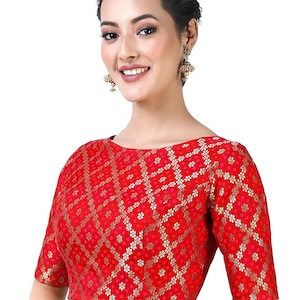 May include: A red brocade blouse with a floral pattern and gold accents. The blouse has a round neckline and short sleeves.