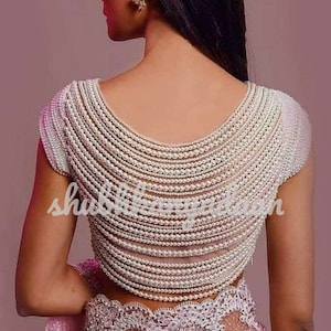 May include: A white blouse with a pearl-embellished back. The pearls are arranged in rows, creating a cascading effect. The blouse has short sleeves and a scoop neckline.