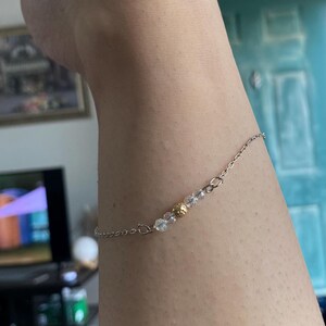 Pode incluir: Um tornozelo de corrente de prata com contas transparentes e douradas.