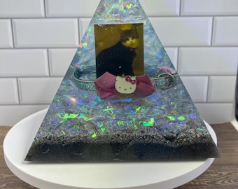 May include: A clear iridescent pyramid with a black and white photo of a cat inside. The pyramid is filled with iridescent glitter and a pink Hello Kitty bow.