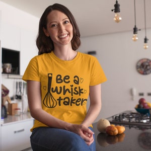 Könnte beinhalten: Ein gelbes T-Shirt mit einer schwarzen Grafik, auf der "Be a whisk taker" mit einer Schneebesen-Illustration und Herzen steht.