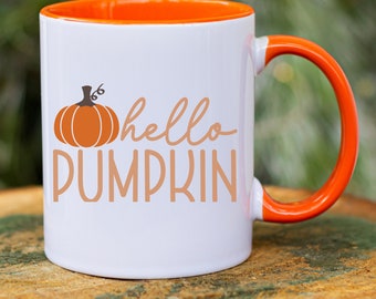 Pode incluir: Caneca de cerâmica branca com borda e alça laranja. A caneca tem uma abóbora laranja e o texto "hello pumpkin" impresso nela.