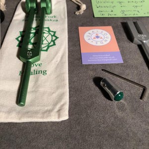 K&ouml;nnte beinhalten: Ein gr&uuml;ner Stimmgabel mit einer wei&szlig;en Tasche und einer Visitenkarte. Die Stimmgabel ist mit "FA 528 3/4" und "Love Healing" beschriftet. Die Visitenkarte ist f&uuml;r "Aura Sounds" und hat eine Website und eine E-Mail-Adresse.