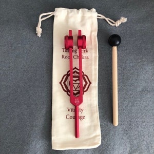 May include: A red tuning fork with a wooden mallet, labeled "UT 285 1/1", "Tuning Fork Root Chakra", "Vitality Courage".