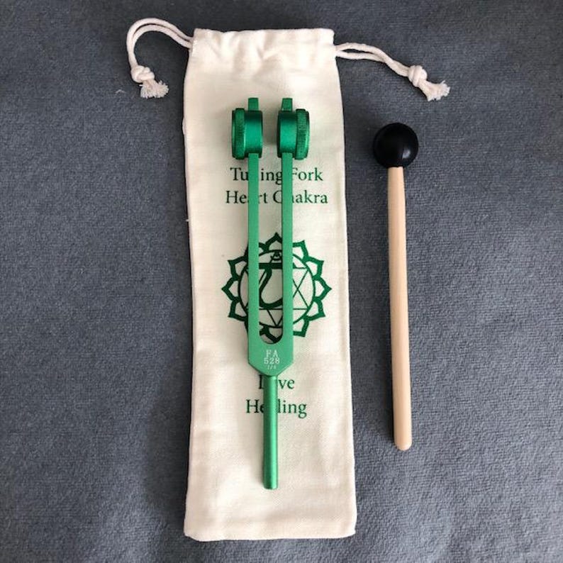 K&ouml;nnte beinhalten: Gr&uuml;ne Stimmgabel mit einer wei&szlig;en Tasche und einem Holzhammer. Die Stimmgabel ist mit "Herzchakra" und "FA 528 Hz" beschriftet.