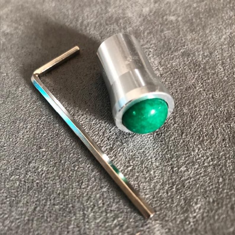 K&ouml;nnte beinhalten: Ein silberner Metallknopf mit einer gr&uuml;nen Edelsteinoberseite und einem silbernen Inbusschl&uuml;ssel.