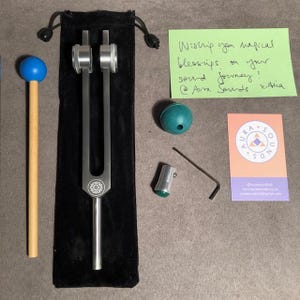 May include: A silver tuning fork with a black velvet pouch, a wooden mallet with a blue rubber head, a green ball, a silver tuning fork activator, a silver Allen wrench, and a business card for Aura Sounds.