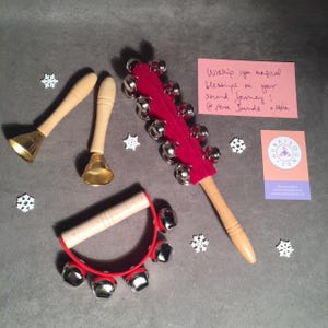Può includere: Strumenti musicali: due campane in ottone con manici in legno, un bastone tintinnante rosso e argento e un tamburello rosso. Sono presenti anche un biglietto rosa con testo scritto a mano e un biglietto da visita.