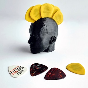 May include: A black 3D-printed head sculpture with yellow guitar picks arranged to resemble a mohawk. Three guitar picks are at the base of the sculpture, one with the text "ABBEY ROAD NW8 WESTMINSTER".