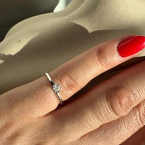 Puede incluir: Un anillo de banda de plata simple con un solo diamante redondo pequeño.