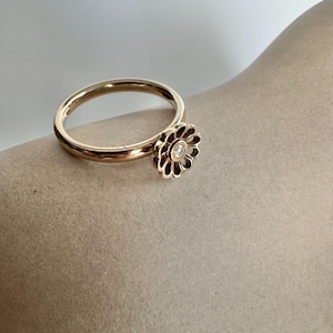 Puede incluir: Un anillo de oro con un delicado diseño de flor y un pequeño diamante en el centro.