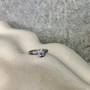 Puede incluir: Un anillo de plata con un diseño de flor blanca. La flor está hecha de pequeñas piedras blancas.