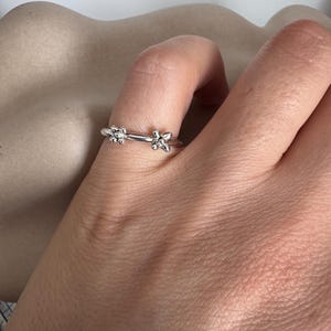 Puede incluir: Un anillo de plata con dos pequeños diseños de flores en la banda.
