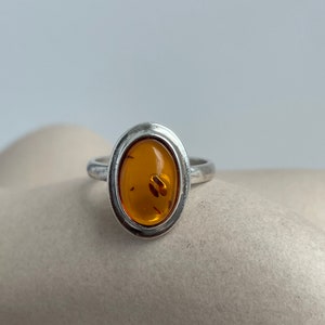 May include: A silver ring with an oval amber stone set in a bezel setting.