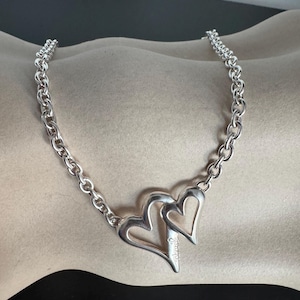 May include: A silver chain necklace with a double heart pendant. The pendant is inscribed with the word "Schulte".