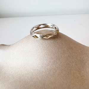 Puede incluir: Un anillo de plata con un diseño geométrico. El anillo está hecho de metal texturizado y tiene un acabado cepillado.