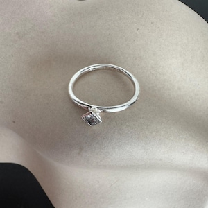 Puede incluir: Un anillo de plata con una piedra transparente de forma cuadrada engastada en la banda.