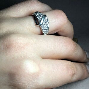 May include: A silver ring with a criss-cross design and small clear stones.