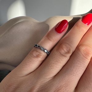 Puede incluir: Un anillo de plata con un delicado diseño de cadena adornado con pequeñas piedras negras.